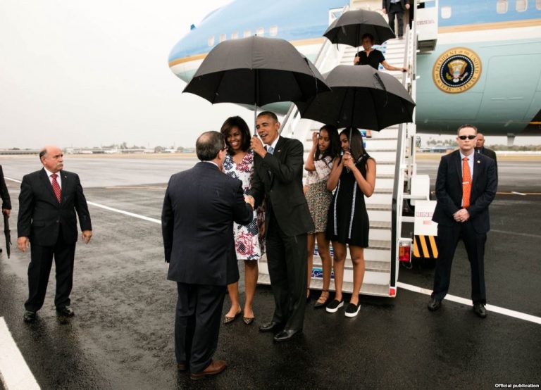 A picture of Barack and Michelle Obama greeting a Cuban official. Obama's two daughters stand behind Barack Obama.