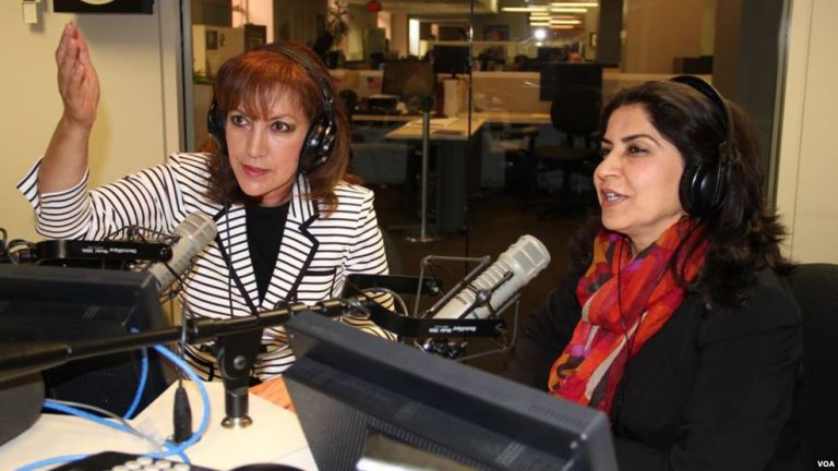 Two women speak in front of a microphone in a radio studio.