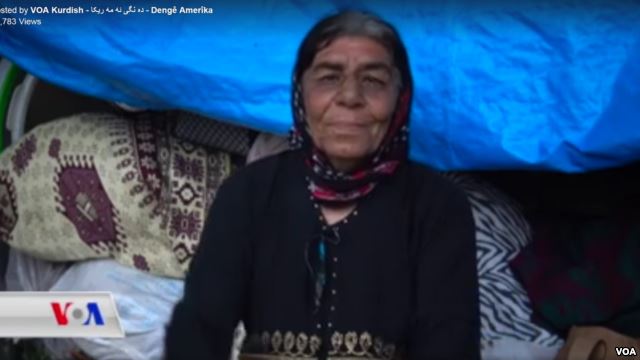 Close up of woman wearing headscarf. She sits in a tent with traditional carpets behind.