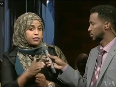 A woman on the left speaks into a microphone held by a man on the right.