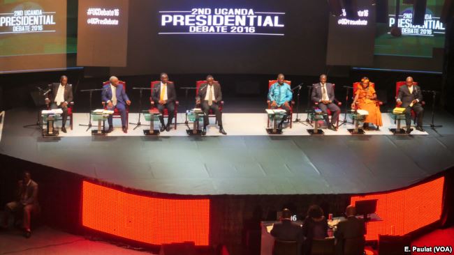 Eight men and women sit in front of a screen displaying "2nd Uganda Presidential Debate 2016."