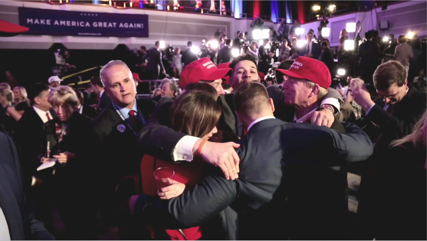 Members of a group, some wearing "Make America Great Again" hats, hug each other