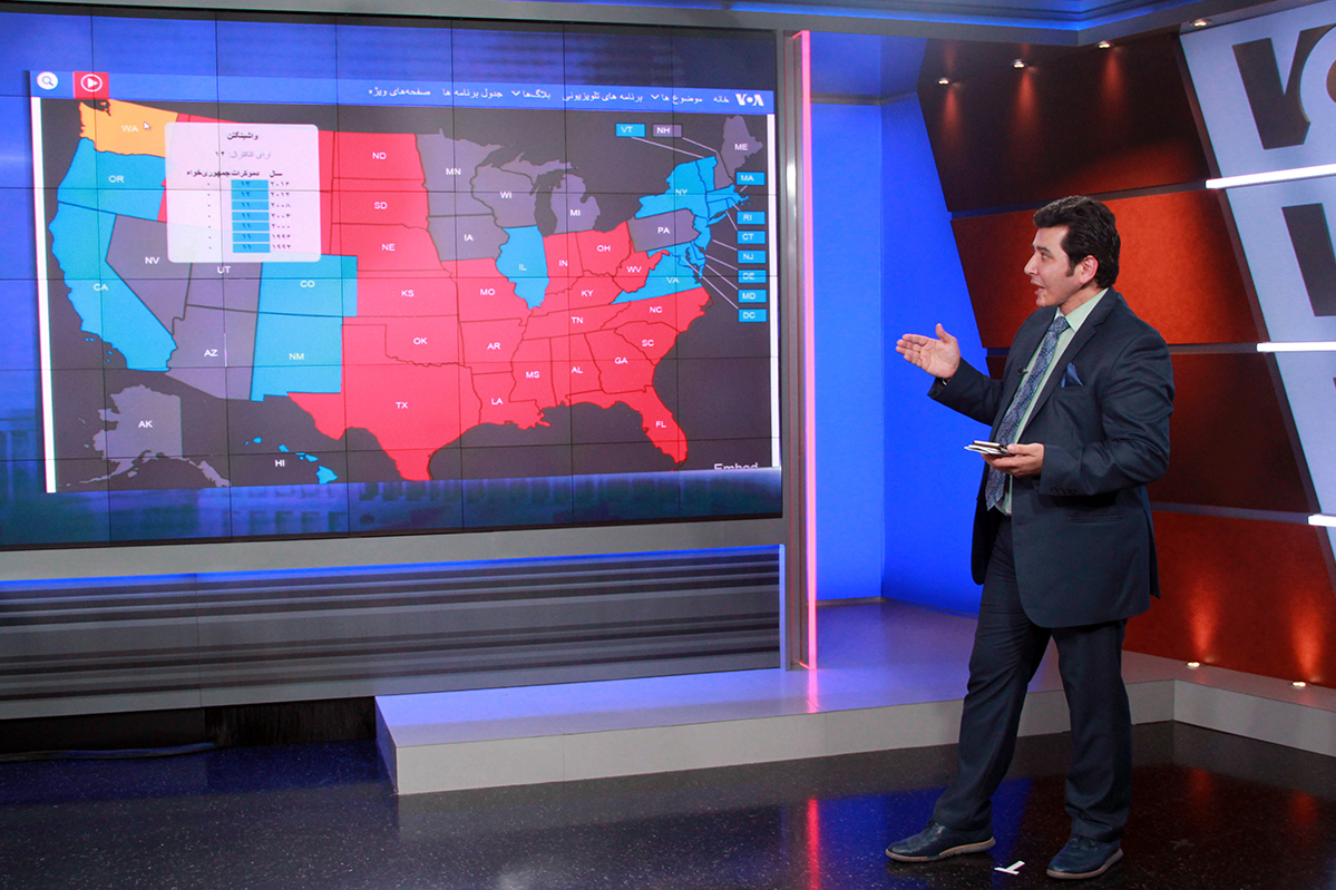 A man reports in front of a screen showing an electoral map.