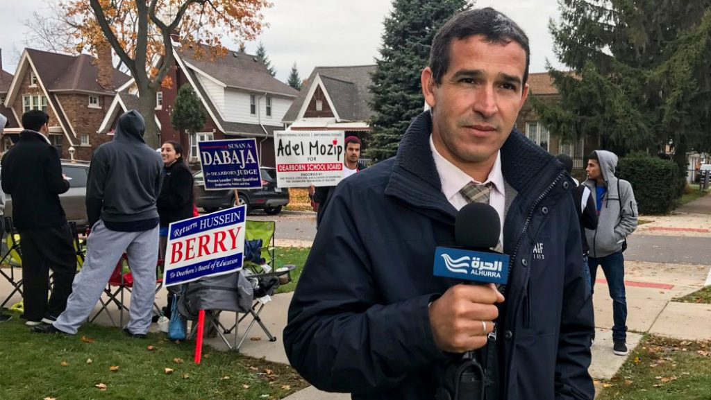 A man holds an Alhurra microphone in front of campaign signs.