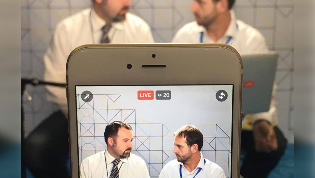 An iPhone screen showing a Facebook live video of two men talking.
